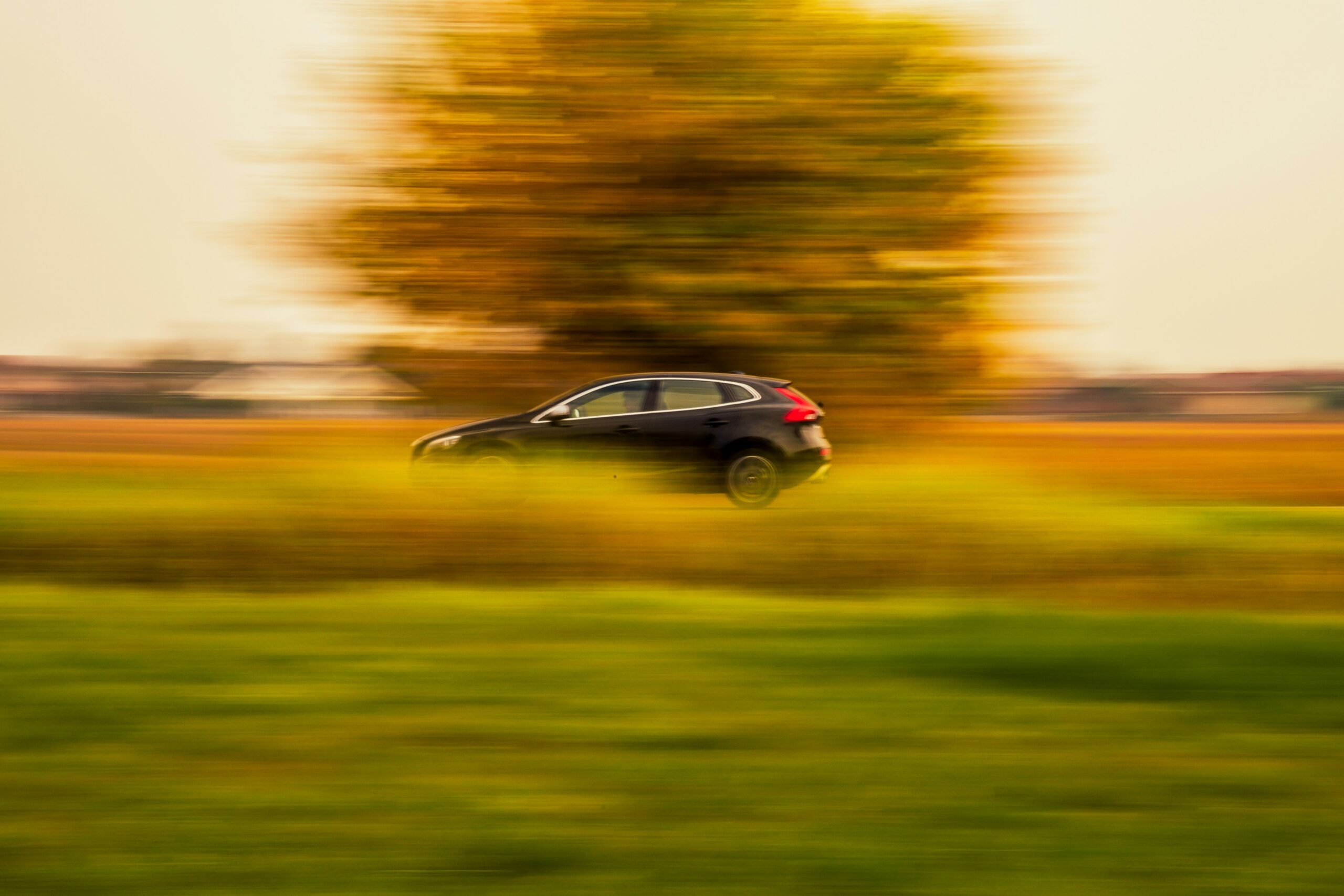 A black car speeds past a blurred golden autumn backdrop