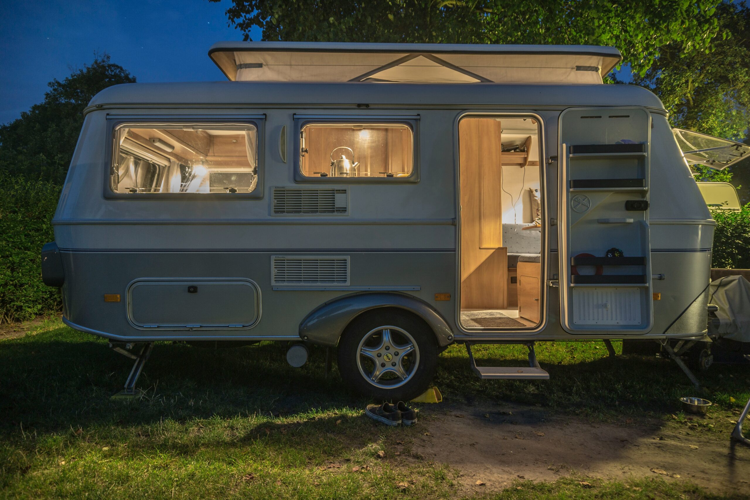 A caravan with its door open, warmly lit inside during nighttime camping