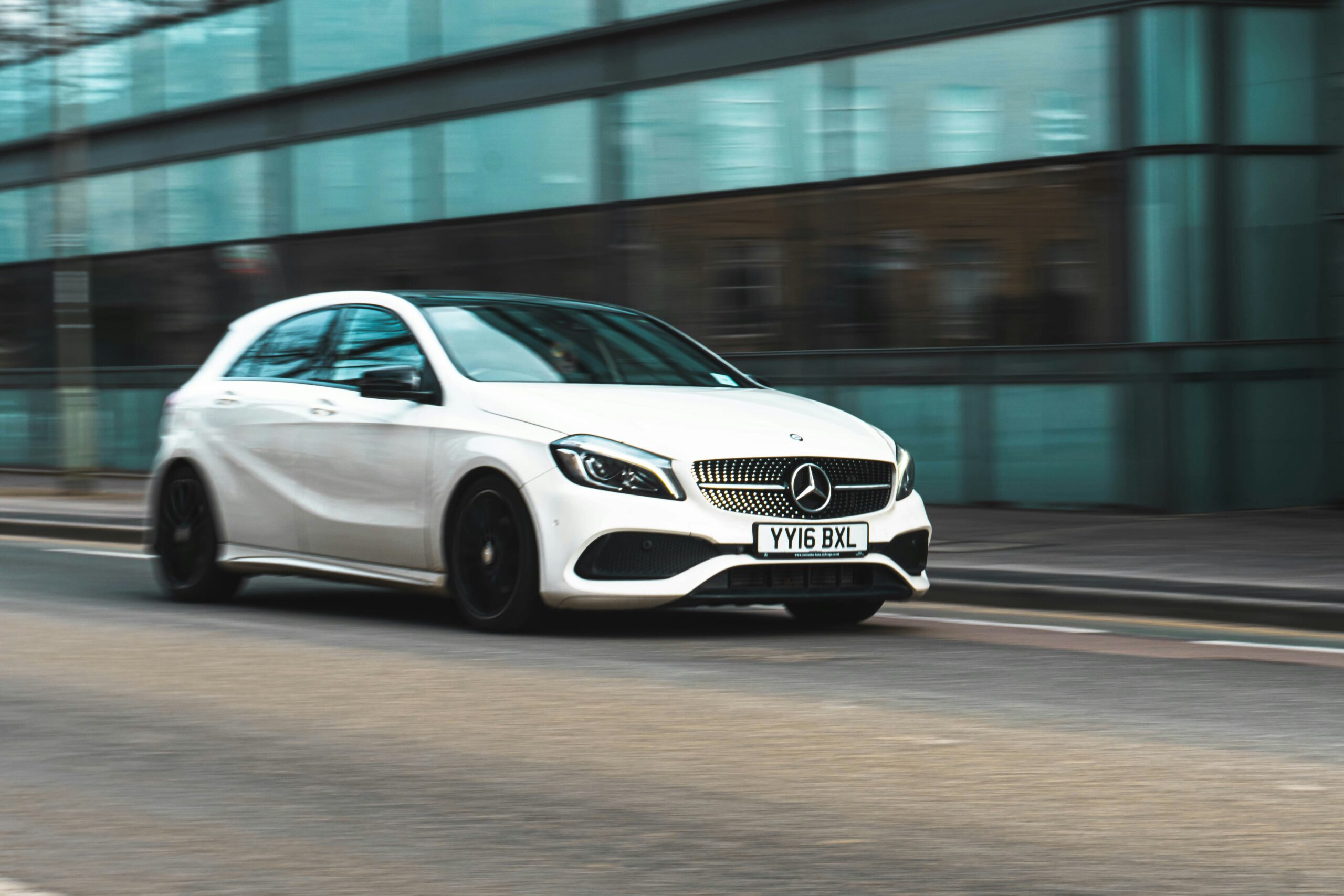 White Mercedes-Benz hatchback driving on a city street in motion